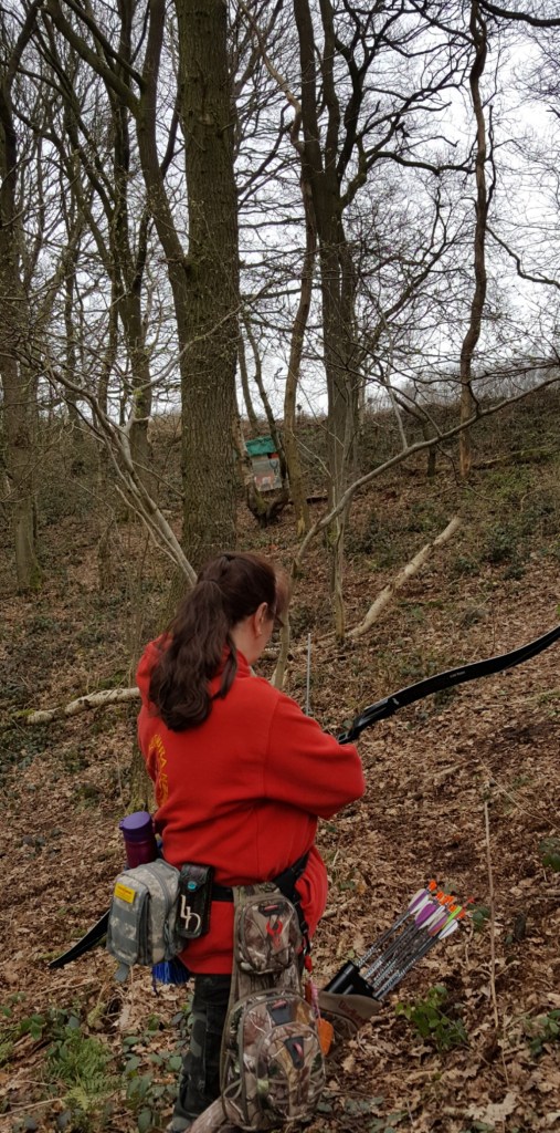 Lynne shooting at paper face target between trees and uphill