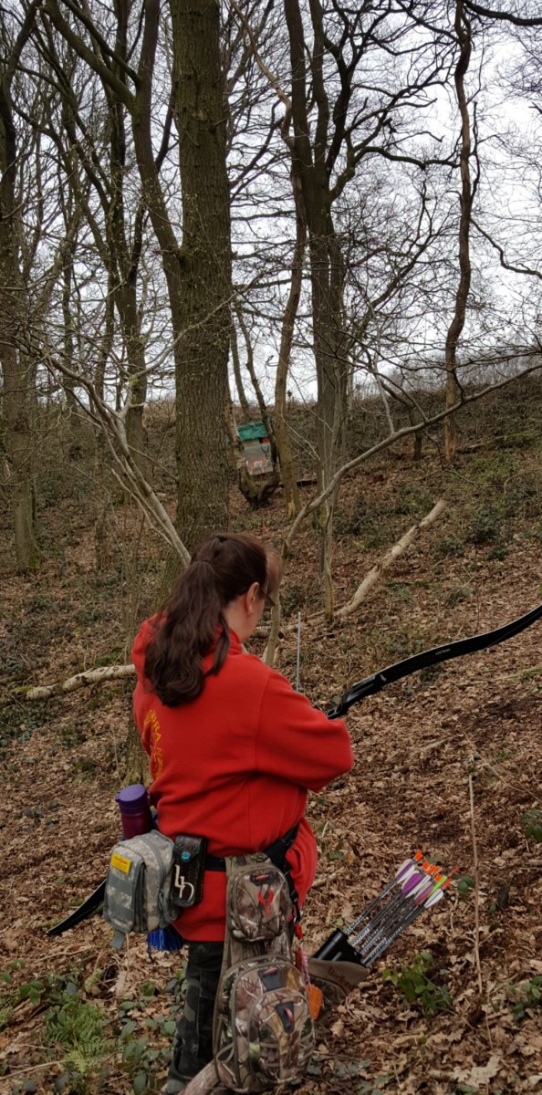 Lynne shooting at paper face target between trees and uphill